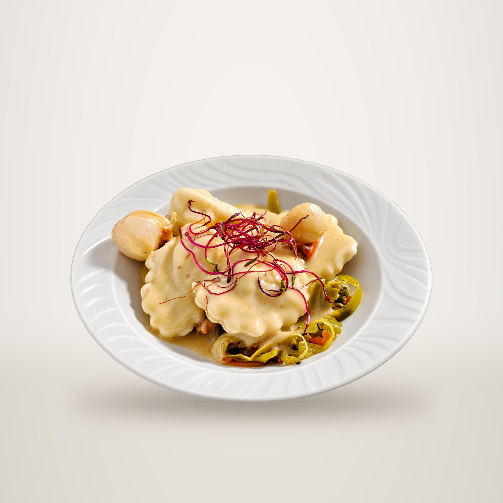 Assiette de raviolis nappés de crème, garnie d’oignons grelots et de pousses rouges.