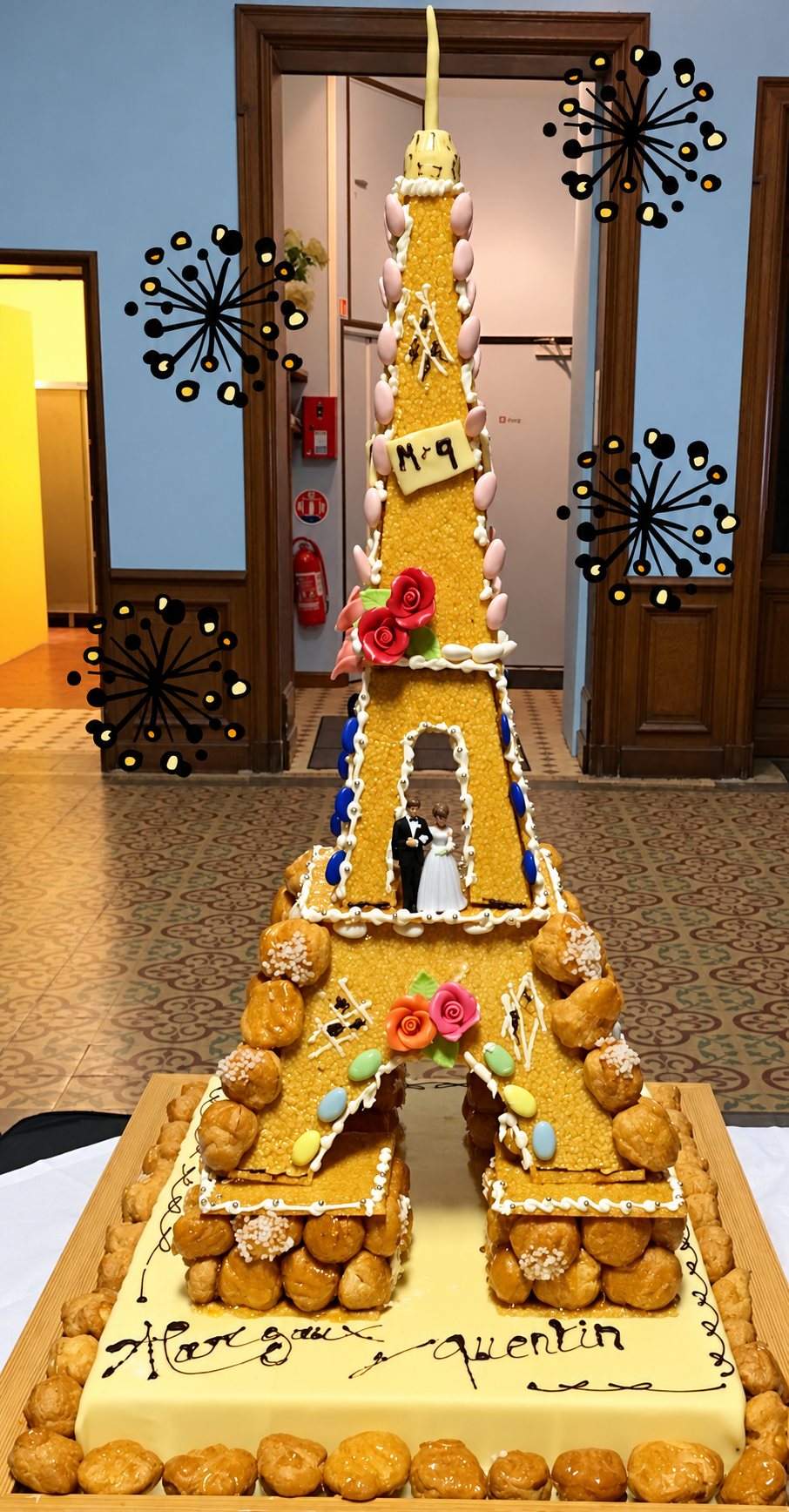 Une pièce montée de mariage en forme de tour Eiffel, faite de choux caramélisés, de dragées et de roses en sucre, avec les prénoms des mariés inscrits sur la base.